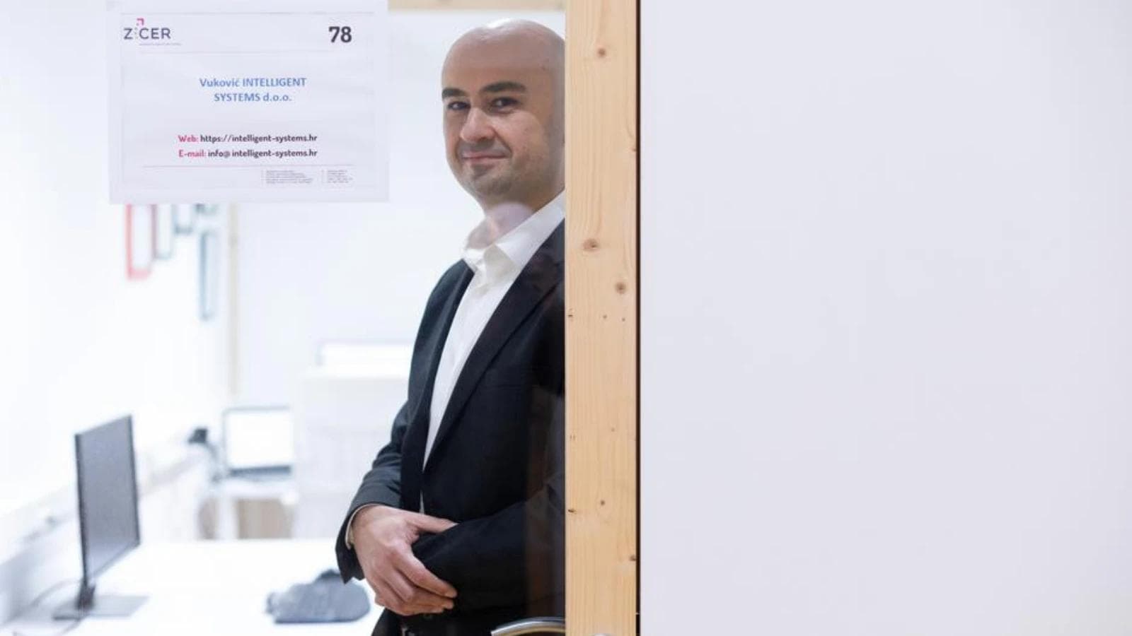 A man in a suit standing by an office door with a ZICER sign.