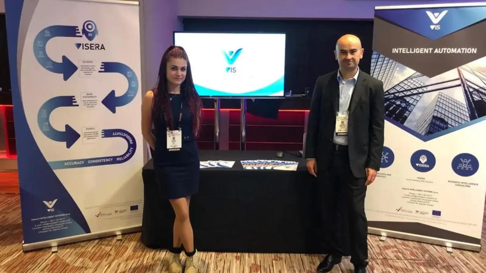 Business woman and man presenting VIS intelligent automation solutions at a technology conference exhibition.
