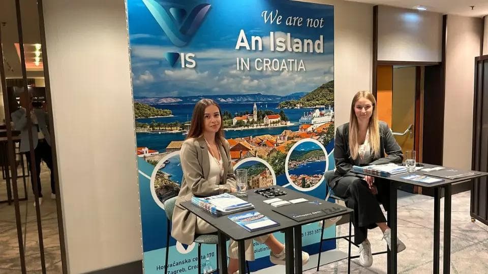 Two women sitting at a VIS promotional booth at an event in Vienna.